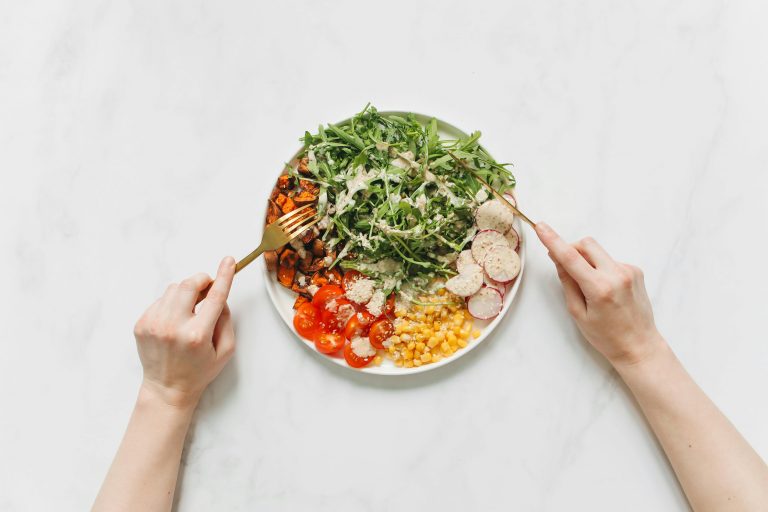 Top view of a colorful and nutritious vegetable salad with hands holding forks.